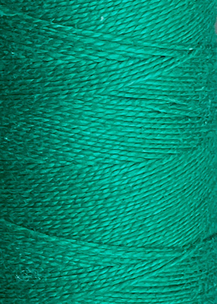 Close-up view of tightly wound, bright teal green 3/2 Looma Circulo Mercerized Pearl Cotton Yarn | Mini Cone by Circulo, highlighting the texture and individual fibers arranged in a diagonal pattern.
