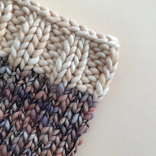 Close-up of a knitted fabric sample from the Aguas Blancas Cowl Pattern by Kristel Nieves for Ravelry Instore, featuring chunky merino wool in gradient cream, purple, and brown hues—ideal inspiration for your next cozy knit.