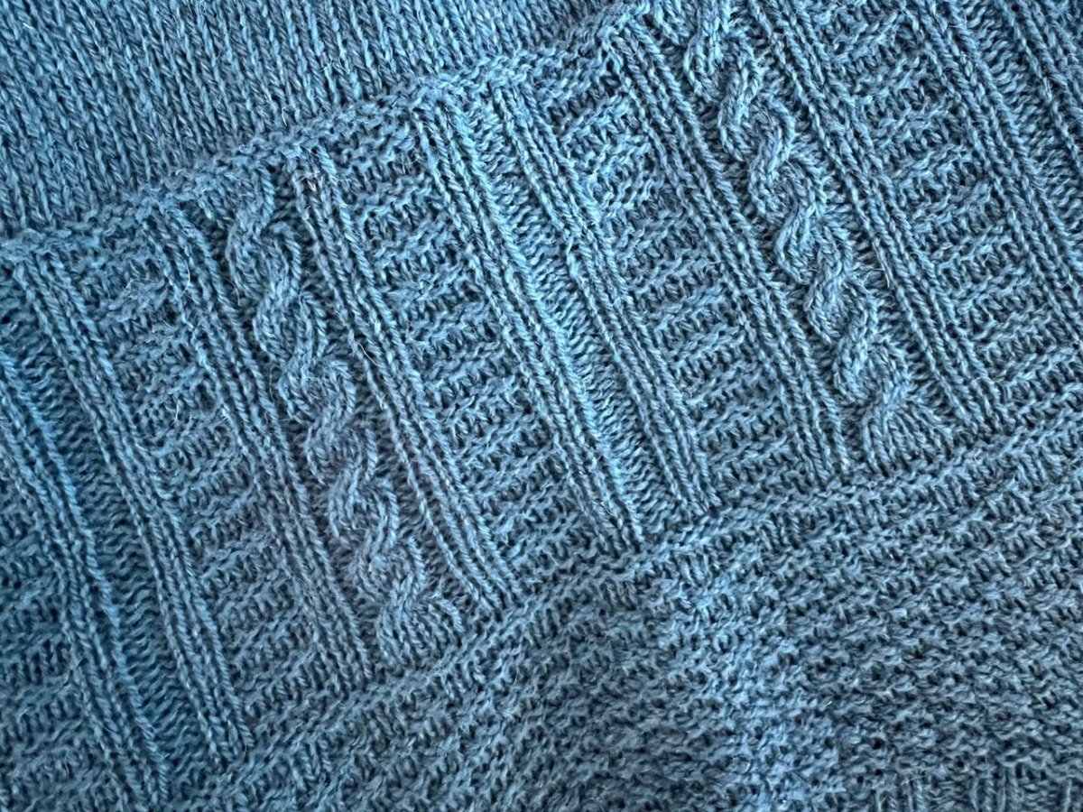 Close-up of blue knitted fabric with vertical ribs and cable stitches, inspired by traditional gansey sweaters. Discover hand-dyed yarns and finished ganseys at the Pop-up Sale with Linda Perry by Halcyon Yarn on Saturday, May 23rd.