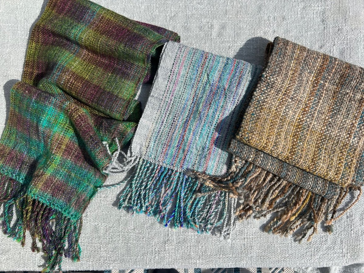 Three handwoven scarves from Halcyon Yarn are displayed side by side, each with unique colors and fringed ends. Join our Weaving Demo + Pop-Up Shop to benefit Oasis Free Clinic, Friday & Saturday May 8-9 (all day).