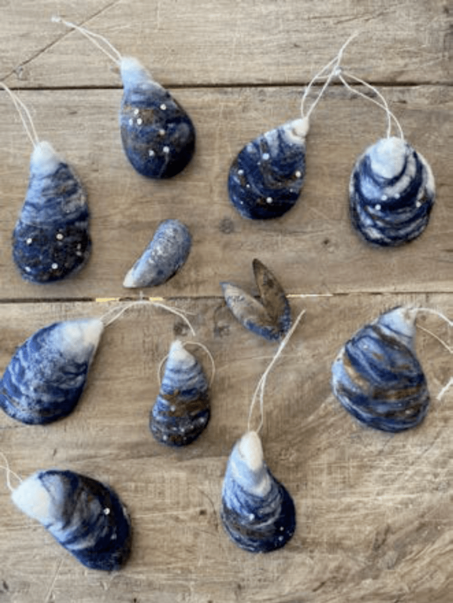 Thirdlee Co’s Thirdlee Maine Needle Felting Kits Mussel Shells feature handmade blue and white felt ornaments with hanging strings, glitter accents, and a real mussel shell, all displayed on a wooden surface.