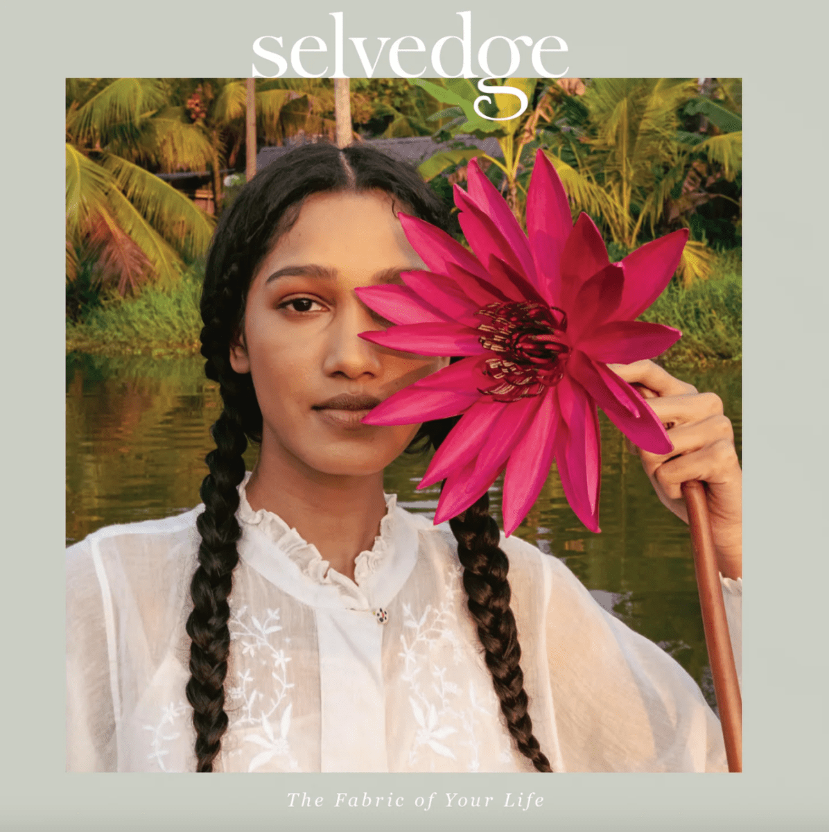 A woman with braided hair in a white blouse holds a large pink flower over one eye, against a backdrop of lush trees and water. The image features "Selvedge" and "Selvedge Issue 131: Flow.