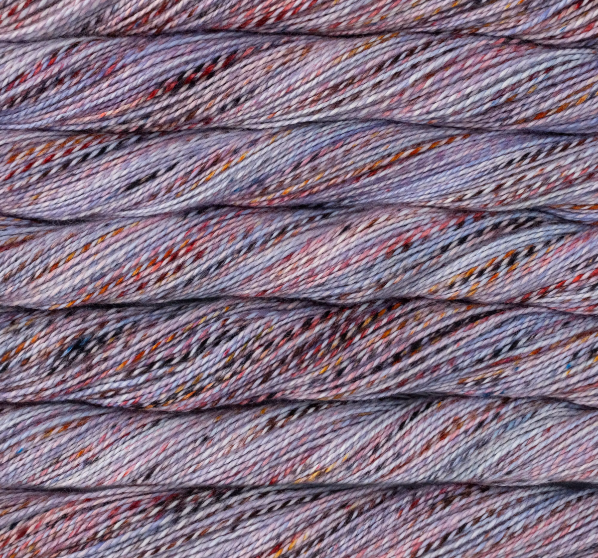 Close-up of Malabrigo Torzal sport weight yarn in variegated shades of purple, blue, and grey with small flecks of orange and black.