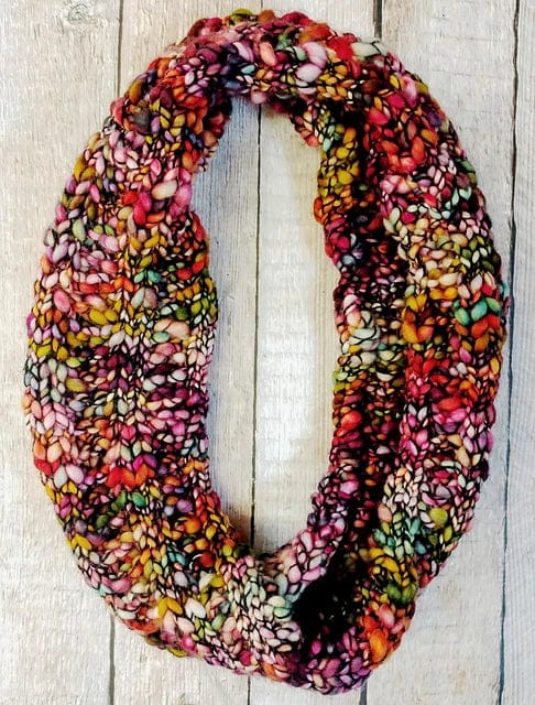 A chunky Malabrigo Caracol knit Veinte Cowl Pattern by Kirsten Hipsky in multicolored yarn shades of pink, yellow, orange, and green.