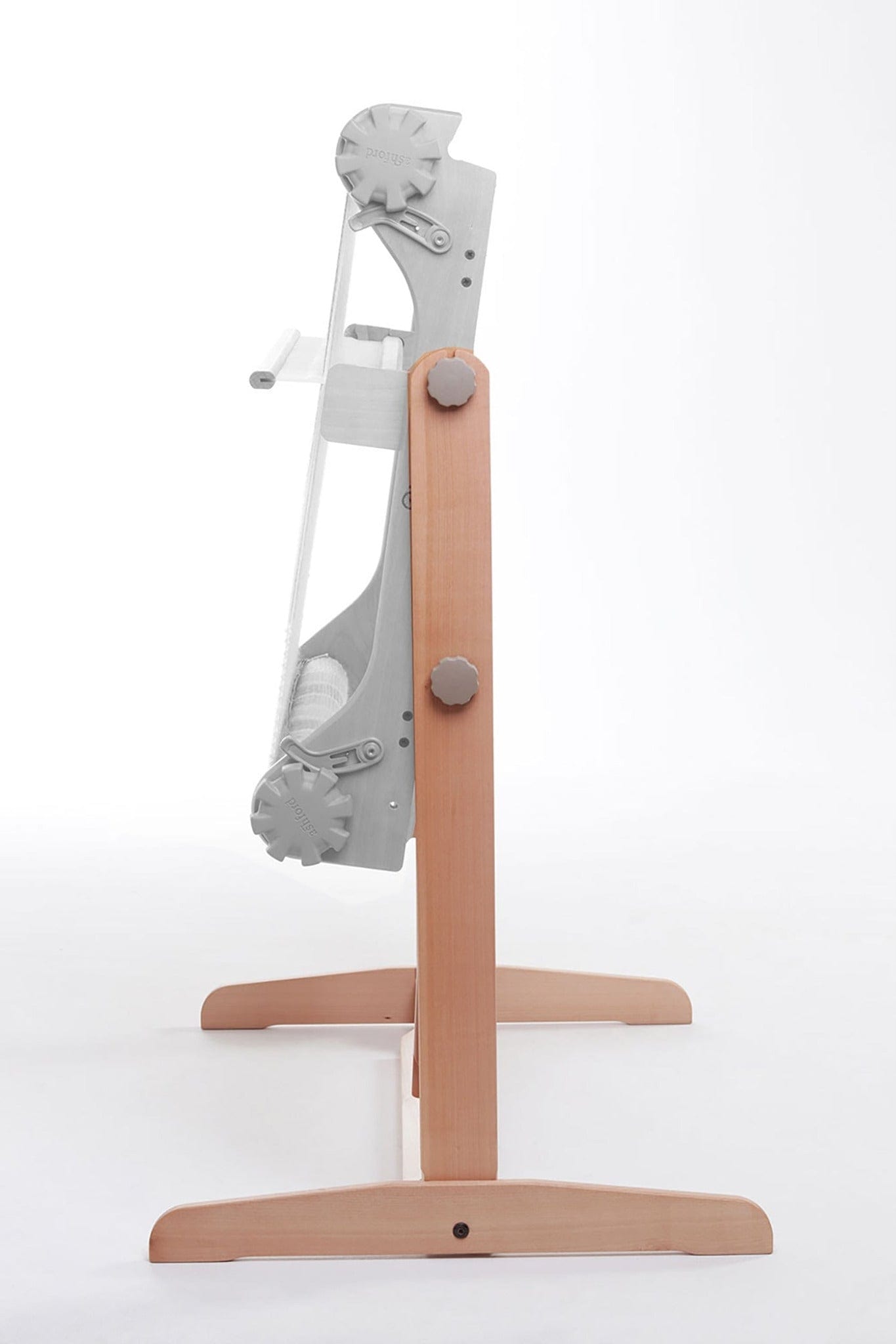 A side view of the Ashford Rigid Heddle Floor Stand by Ashford Handicrafts Limited highlights its wooden base, upright frame with metal parts and handle, and an ergonomic adjustable weaving angle, all set against a white background.