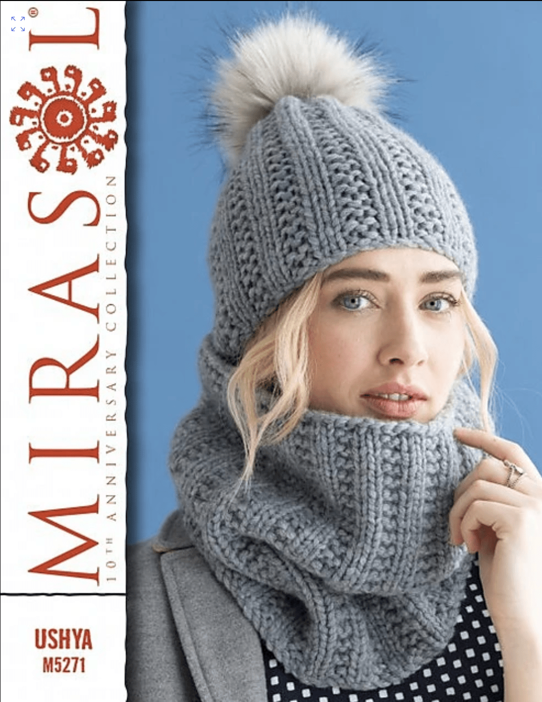 A woman wearing a Cristina Hat & Cowl Pattern by Sandi Prosser, featuring a grey ribbed knit design with a matching pom-pom hat and cowl made from super bulky yarn.