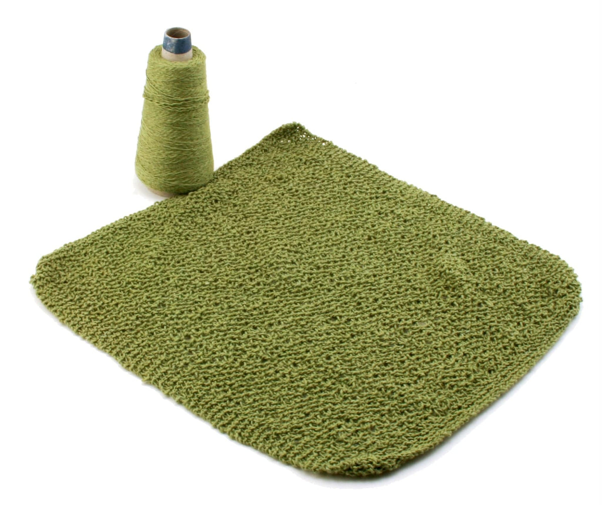 A spool of Halcyon Yarn sits beside a green washcloth knitted from Casco Bay Washcloths by Halcyon Yarn, a downloadable pattern perfect for testing new washcloth designs, displayed on a white background.
