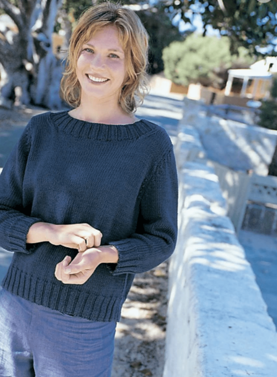 A smiling woman wearing the dark blue, relaxed fit Somerville Sweater by Kingfisher Yarn & Fibre, featuring a ribbed crew neckline and cuffs.