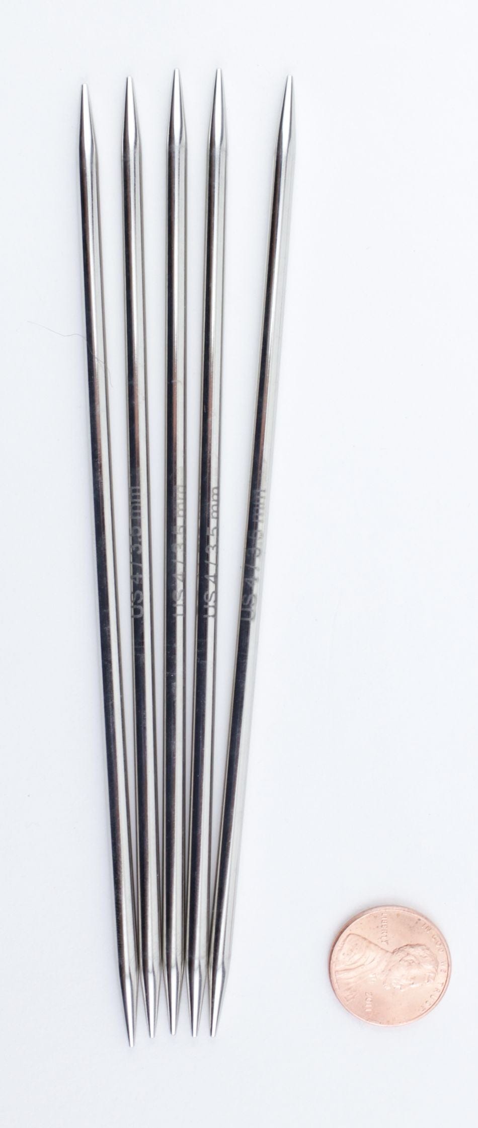 Five Knit Pro (Knitters Pride) Nova Metal 6-inch double-point knitting needles by Accessories Unlimited are lined up on a white background, with a penny nearby for size comparison.