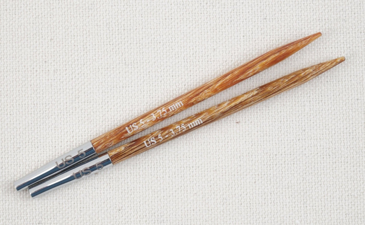 Two Knit Pro (Knitters Pride) Dreamz Interchangeable Knitting Needle Tips by Accessories Unlimited, size US 3/3.25 mm, with metal bases, are shown parallel on a textured light fabric background; made from laminated birch for smooth stitching.
