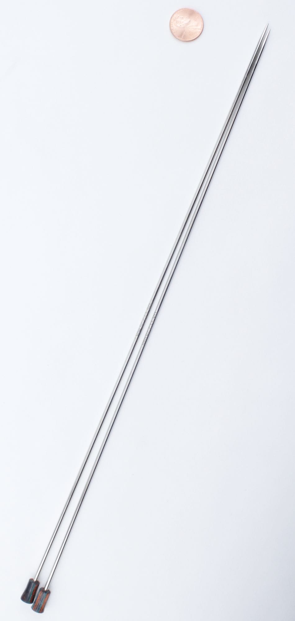 Two long, straight Knit Pro Nova Metal Single Point Knitting Needles by Accessories Unlimited are placed side by side on a white background with a penny above for size comparison.