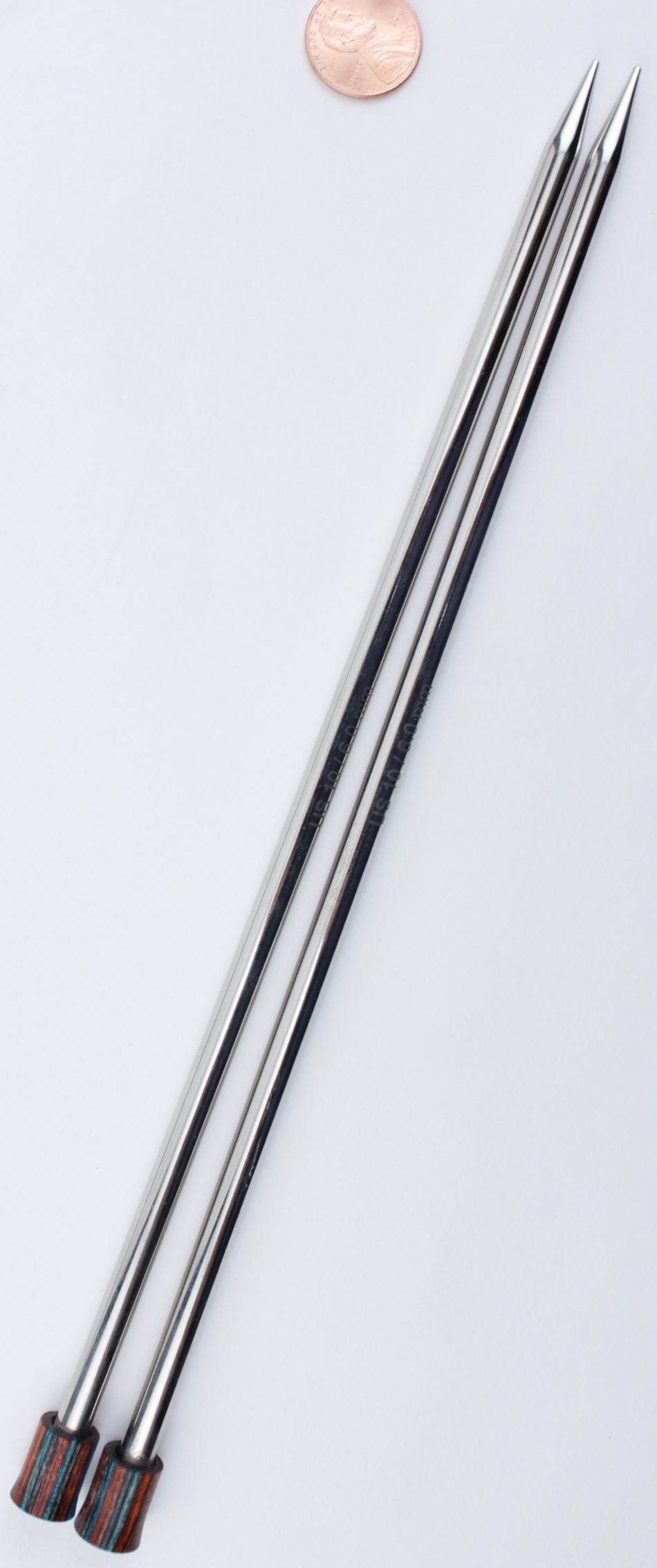Two Knit Pro (Knitters Pride) Nova Metal Single Point Knitting Needles by Accessories Unlimited, each 10" or 14" long with pointed tips and multicolored ends, are arranged side by side on a white surface with a penny above for scale.