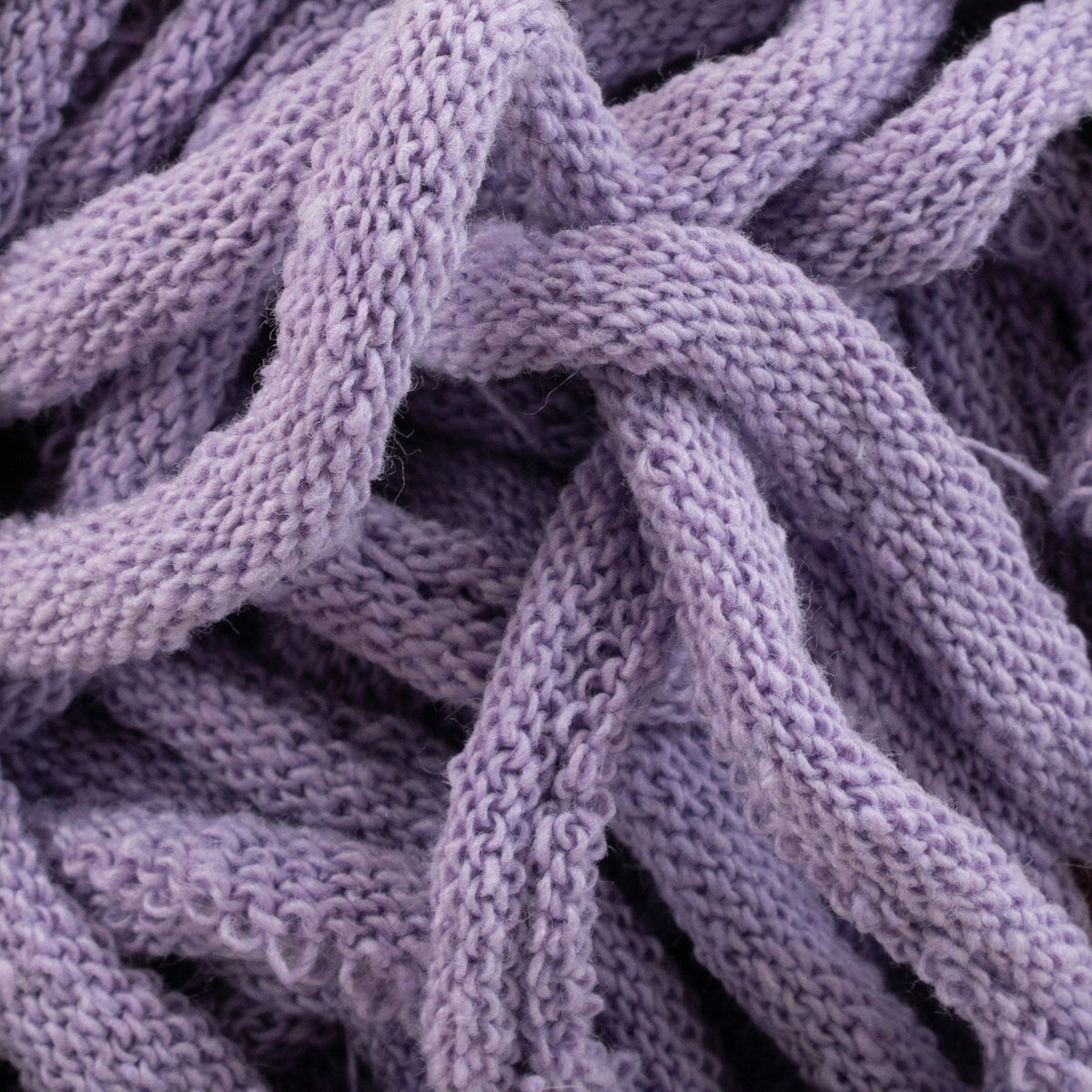Close-up of intertwined strands of Harrisville Potholder Loops by Friendly Loom, in a soft, knitted lavender hue creating a textured pattern reminiscent of a traditional loom. The thick and cozy material suggests it could be used for warm clothing or blankets.