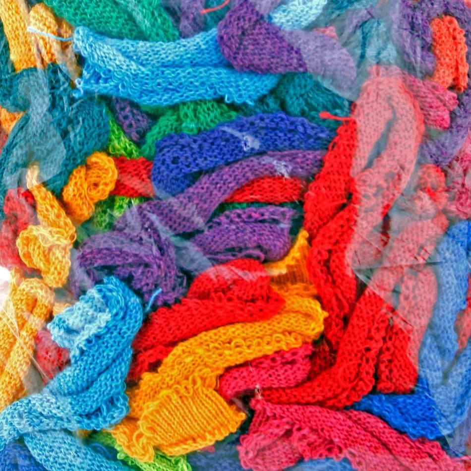 Introducing Harrisville Potholder Loops - Traditional Size by Friendly Loom: A lively collection of knitted fabric strips crafted with a traditional loom, featuring vibrant colors such as red, blue, green, purple, yellow, and orange, all beautifully intertwined and visible through a clear plastic covering.