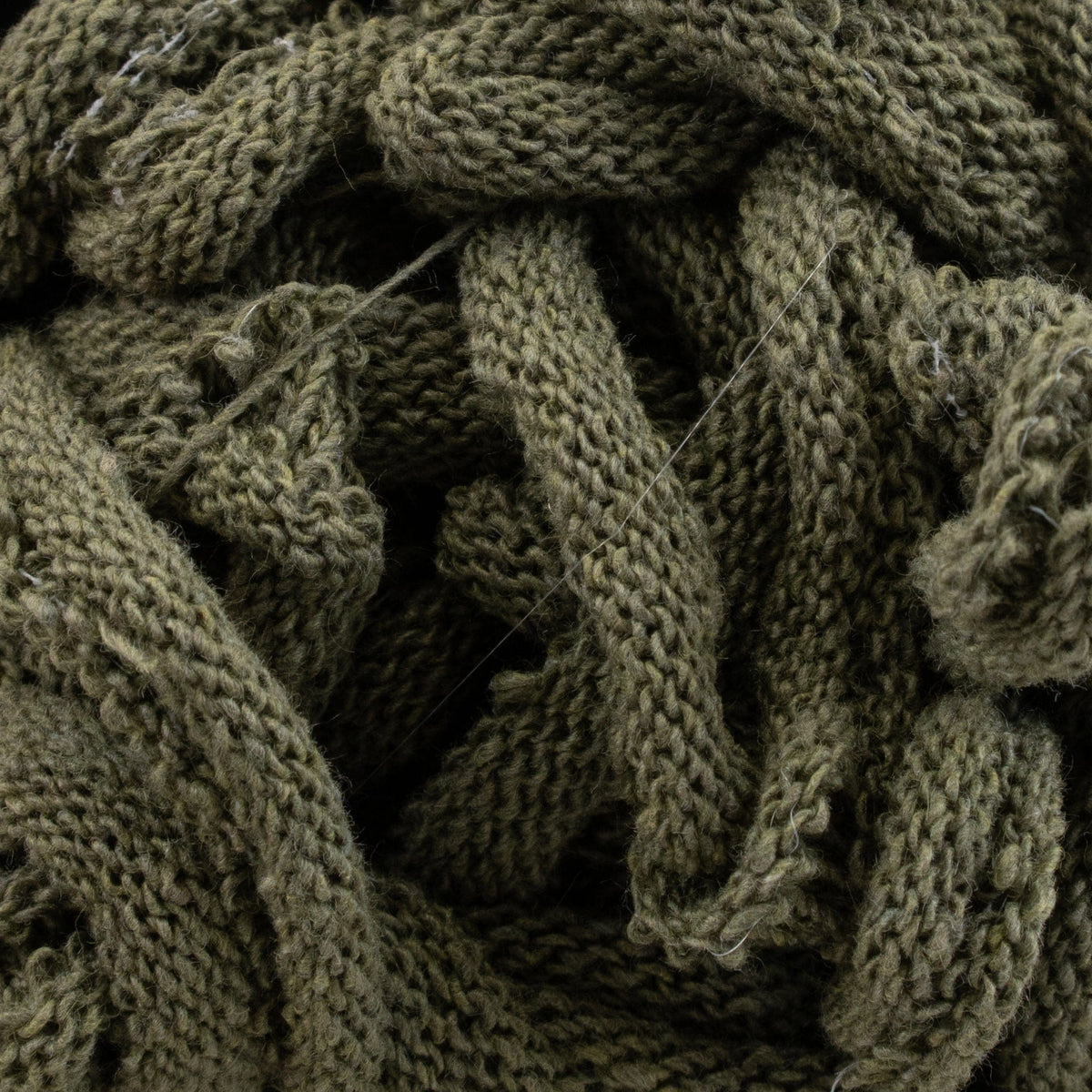 Close-up of tangled, thick, olive-green Harrisville Potholder Loops by Friendly Loom with cotton loops and visible textured stitches, creating a cozy and dense appearance reminiscent of a knit fabric.