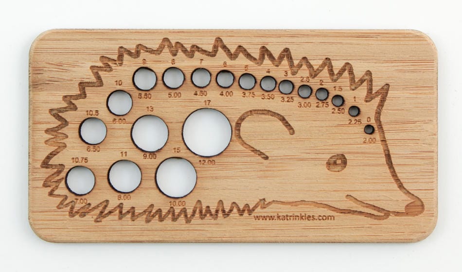 The Katrinkles Animal Needle Gauge is a charming bamboo tool shaped like a hedgehog, with numbered holes for measuring needle sizes and etched details—both practical and cute for knitters.