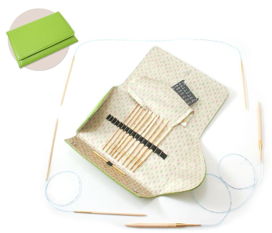 The Skacel Addi-Click Interchangeable Bamboo Needle Set features a green case with bamboo needles, tips, blue cables, and accessories spread on a white surface. An inset displays the closed case—ideal for organizing your interchangeable needles.