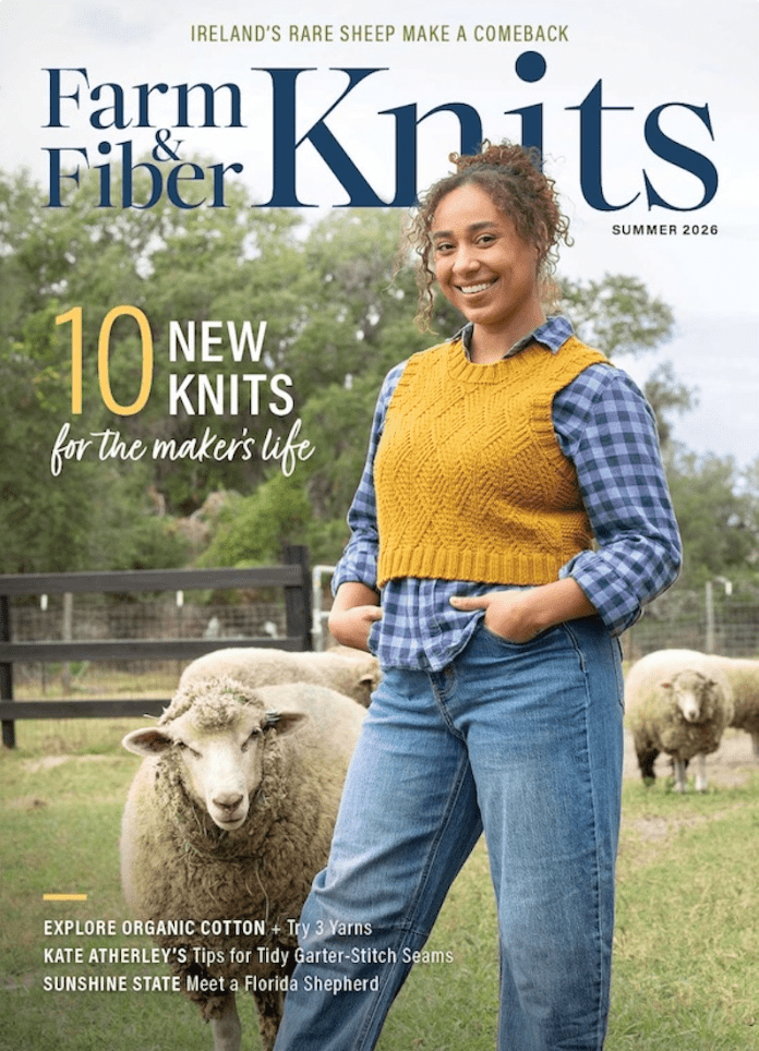 A smiling woman in a yellow knit vest and plaid shirt stands by sheep in a field. The cover shows Farm & Fiber Knits Magazine, Summer 2026 by Long Thread Media, featuring summer fibers, knitting tips, and stories of sheep and yarn.