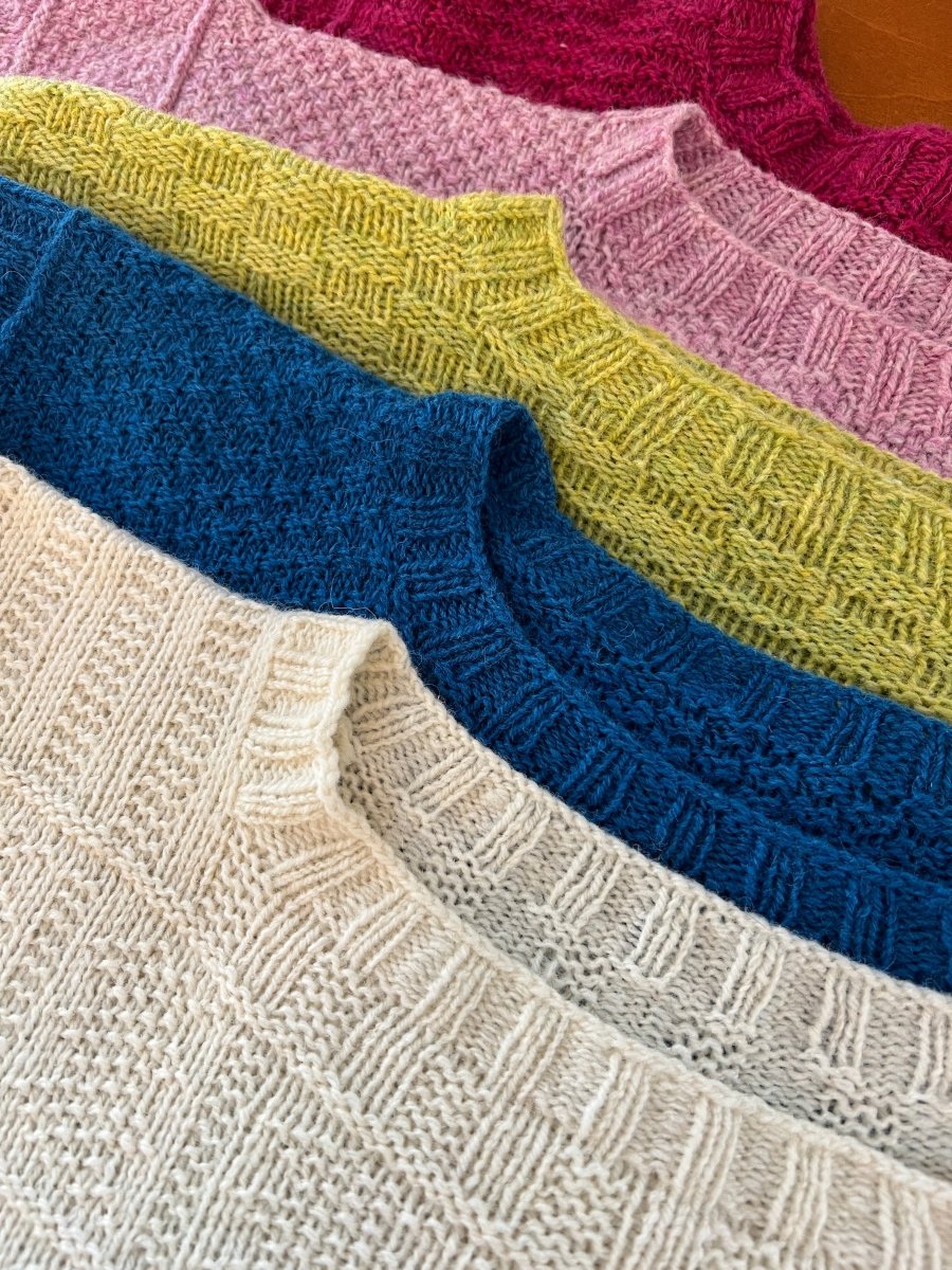 Five knitted sweaters, each in white, blue, yellow-green, light pink, and dark pink, showcase ribbed necklines and textured patterns in Halcyon Yarn’s "The Story of the British Gansey: Artist Talk & Exhibit with Linda Perry" (Aug 6, 2026).