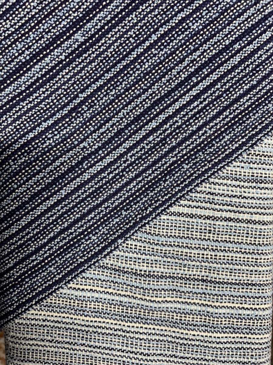 Close-up of two handwoven scarves by Halcyon Yarn: one with dense navy, white, and blue stripes, diagonally over another with lighter, wider lines. See these at the Weaving Demo + Pop-Up Shop for Oasis Free Clinic Benefit, May 8–9.
