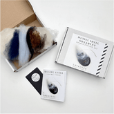 The Thirdlee Co Thirdlee Maine Needle Felting Kits Mussel Shells is displayed with multicolored wool, a box featuring a mussel shell, a "Mussel Shell Instructions" booklet, and a pack of sewing needles.