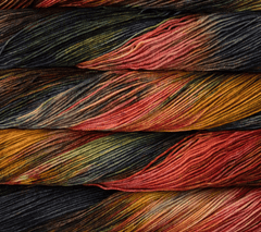 Four stacked hanks of Malabrigo Sock kettle-dyed yarn in shades of dark purple, forest green, amber, and terracotta.
