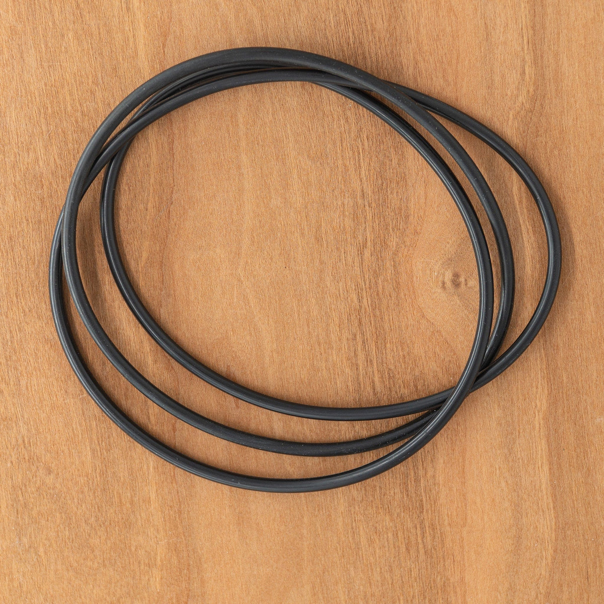 Two black rubber O-rings from the Ashford Drive Band and O-Ring Set for Ball Winder by Ashford Handicrafts Limited are shown overlapping on a light brown wooden surface. Ideal as drive band replacements.