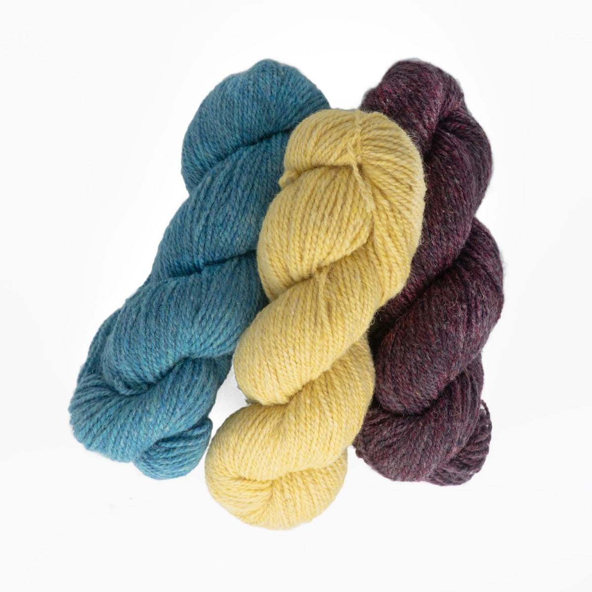 Three skeins of Bartlettyarns Maine Wool Yarn (Fisherman 2-Ply) in teal, yellow, and dark purple are arranged side by side on a white background.