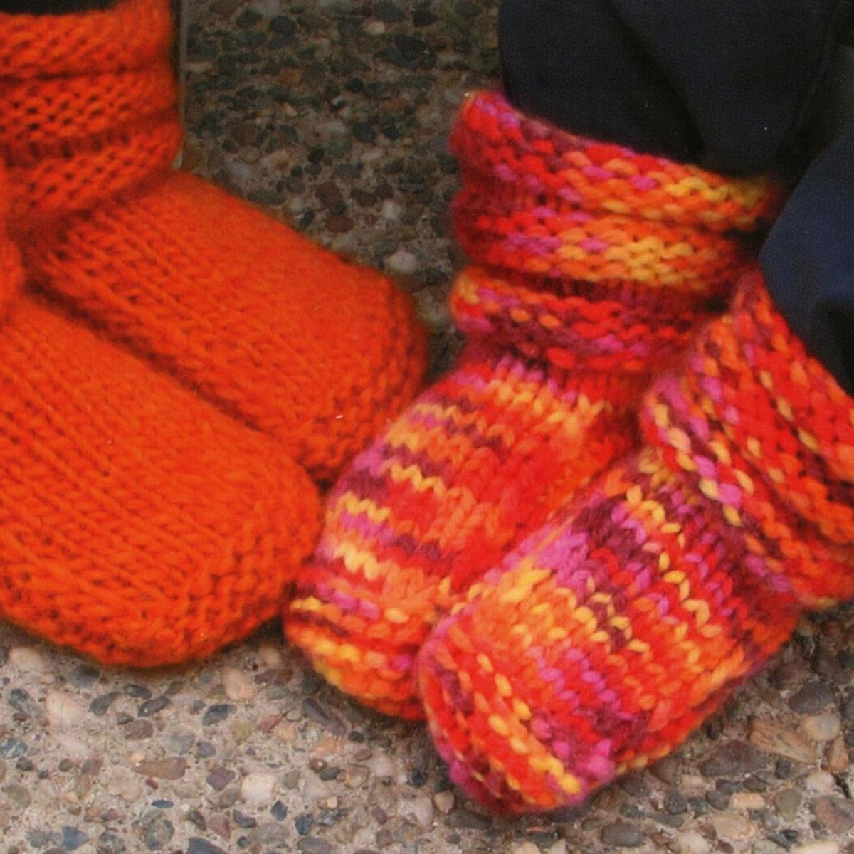 Two pairs of feet in Bryson Distributing, Inc.’s Children’s Mukluk Slippers #113—one bright orange, the other red, orange, and yellow—stand close together on a pebble-textured surface, highlighting their cozy design.