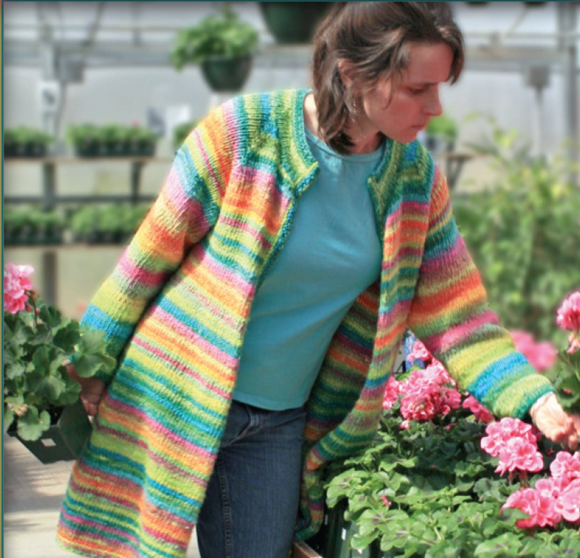 Wearing the Bryson Distributing, Inc. Neck Down Swing Coat (#285), a woman in a colorful, striped cardigan and blue shirt admires pink flowers among lush greenery in a greenhouse.