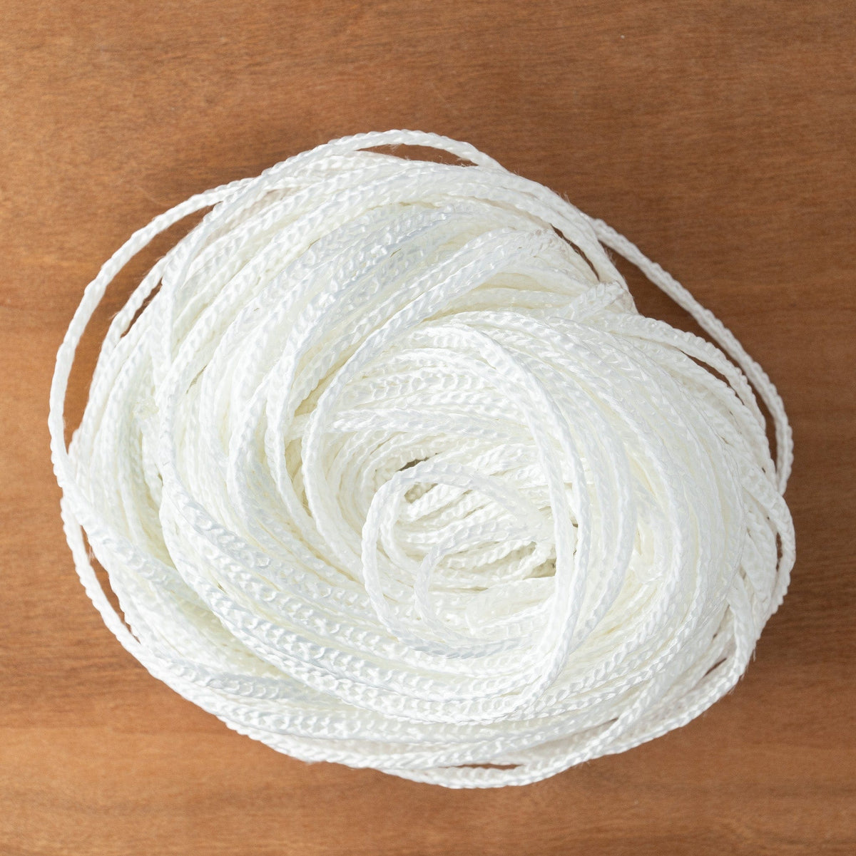 A full spool of Glimakra Texsolv Cord (light loop), containing 22 yards of braided polyester cord, sits neatly coiled on a wooden surface, viewed from above.