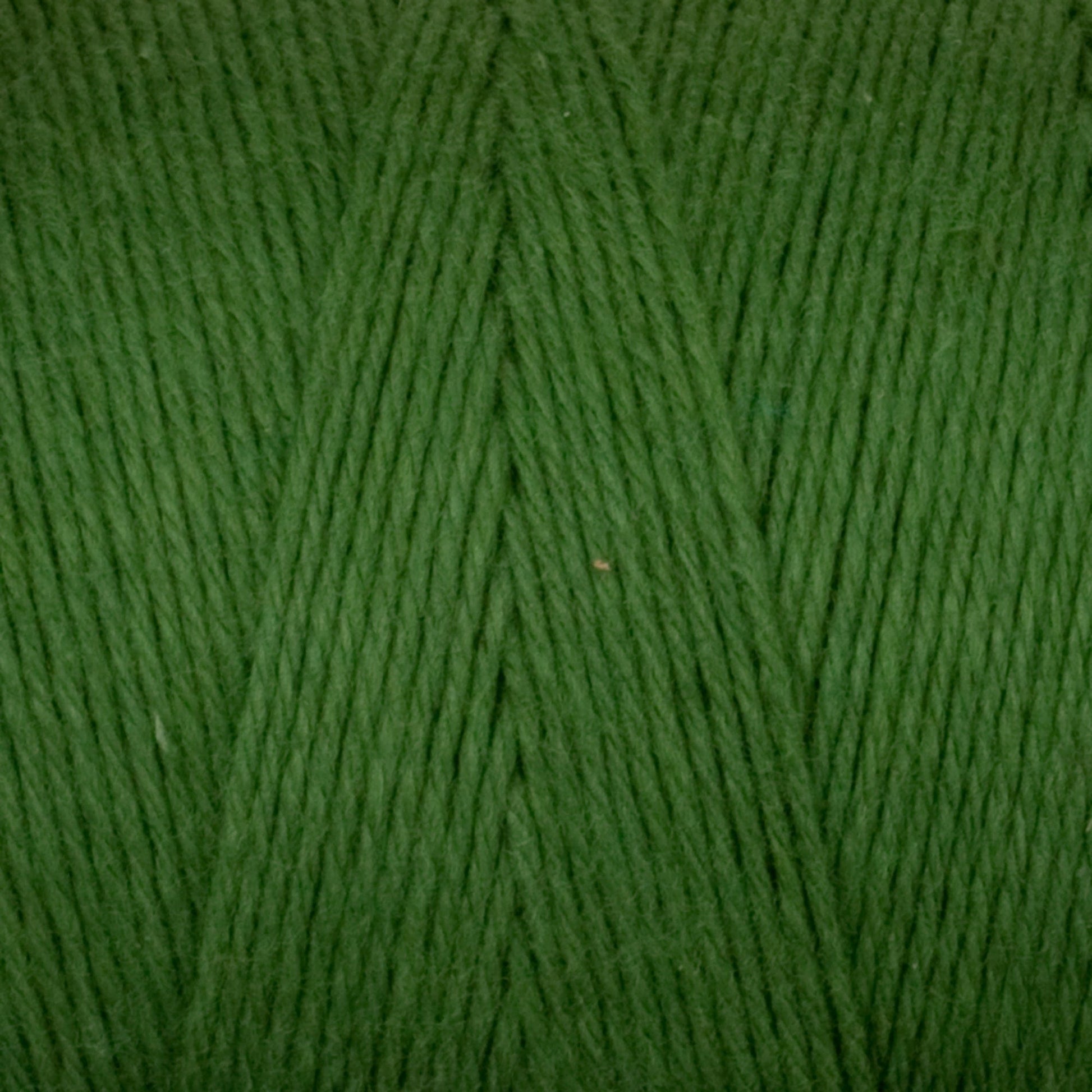 A close-up of Cotton Carpet Warp 8/4 yarn reveals tightly wound green fibers with diagonal lines, offering a soft, slightly shiny texture for a smooth finish—perfect for weaving colorfast rag rugs.