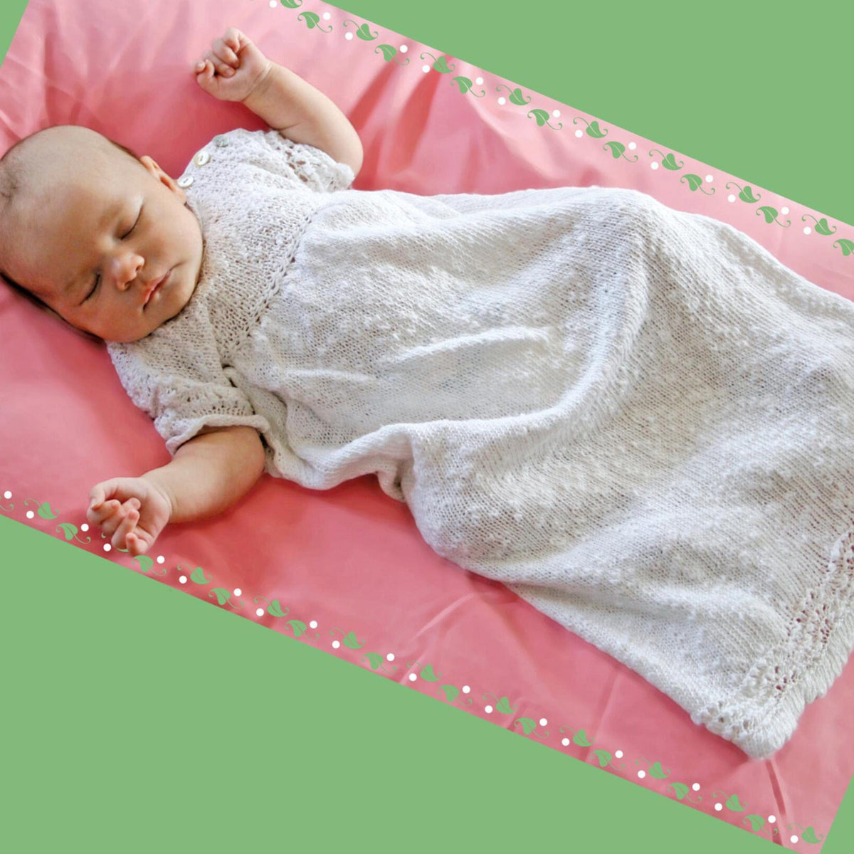 A baby sleeps on a pink blanket in the Halcyon Yarn Heirloom Christening Gown, download; short sleeves and delicate texture shine. A green border with white flowers frames the image, perfectly celebrating new life.