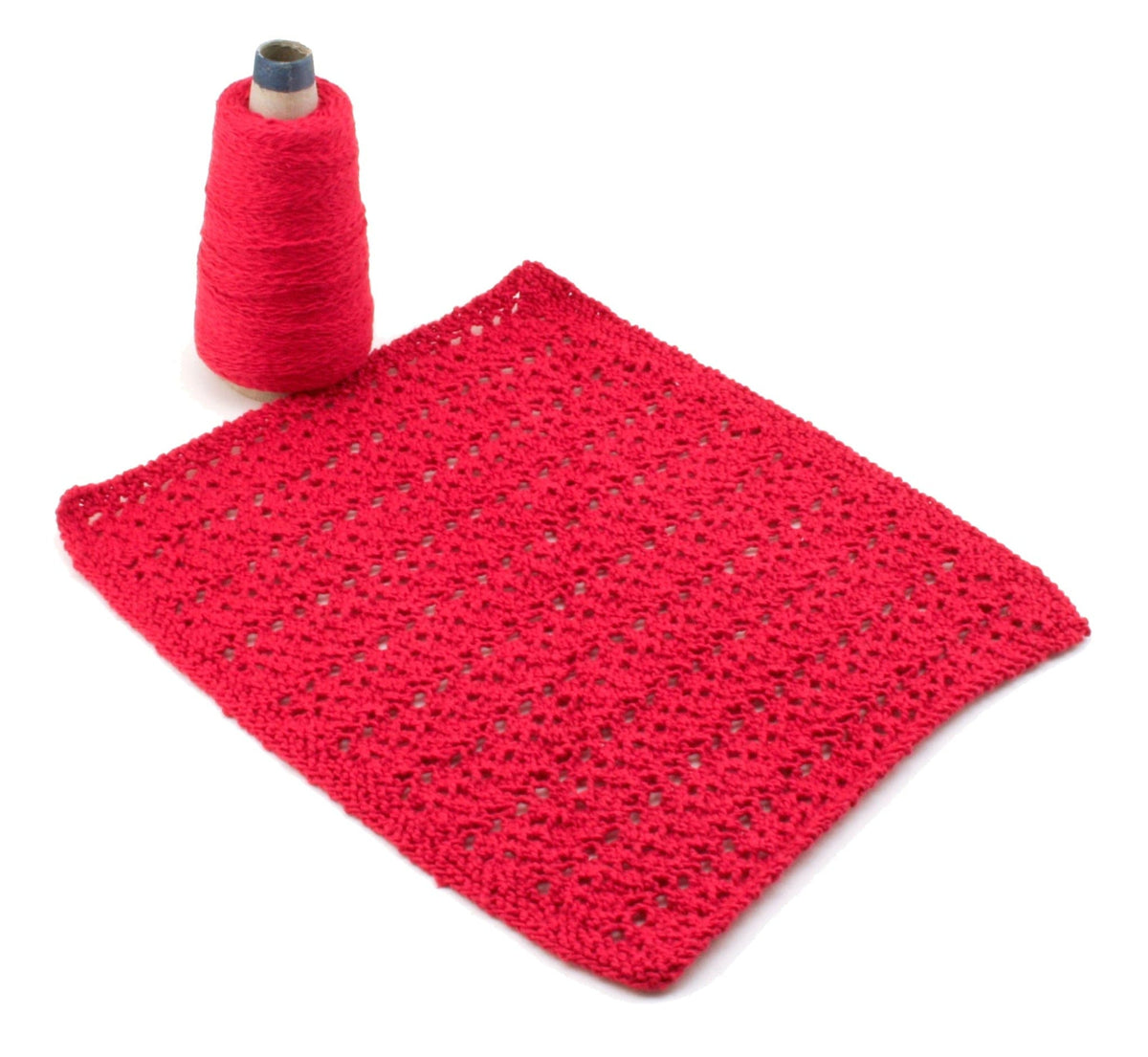 A spool of bright red sport weight cotton yarn is shown beside a lacy, rectangular red crochet fabric made from Halcyon Yarn’s Casco Bay Washcloths pattern (download), all displayed on a white background.