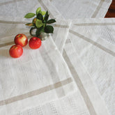 Three red apples and a small glass jar with green leaves rest on Halcyon Yarn’s Classic Newport Linen Towels, which feature delicate lace patterns and beige stripes arranged in an overlapping display.