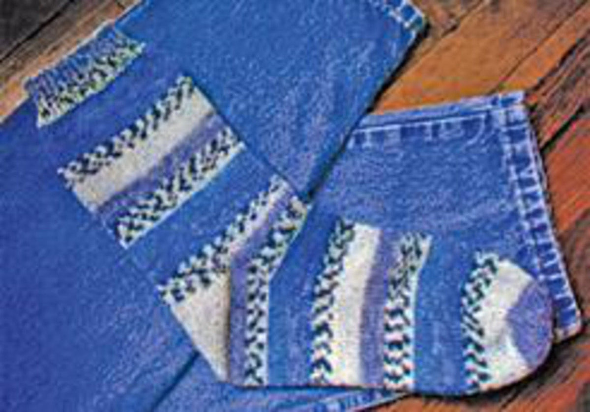 A pair of blue jeans lies on a wooden floor with a sock—knit using Lisa's Knits Basic Toe-Up Sock Pattern (8 st/Inch) in blue, white, and gray sock yarn—placed on one pant leg.