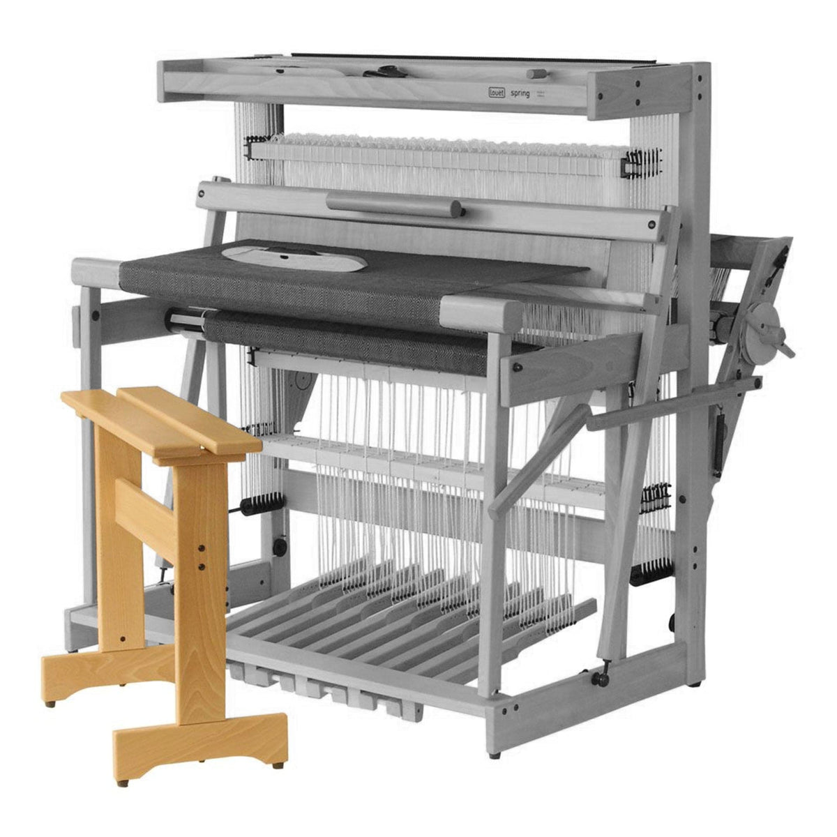 The Louët Loom Bench by Louet Inc. complements a large, multi-shaft floor loom with a gray-toned wooden frame, showcasing warp threads and various levers for weaving. The padded bench features a simple, sturdy design.