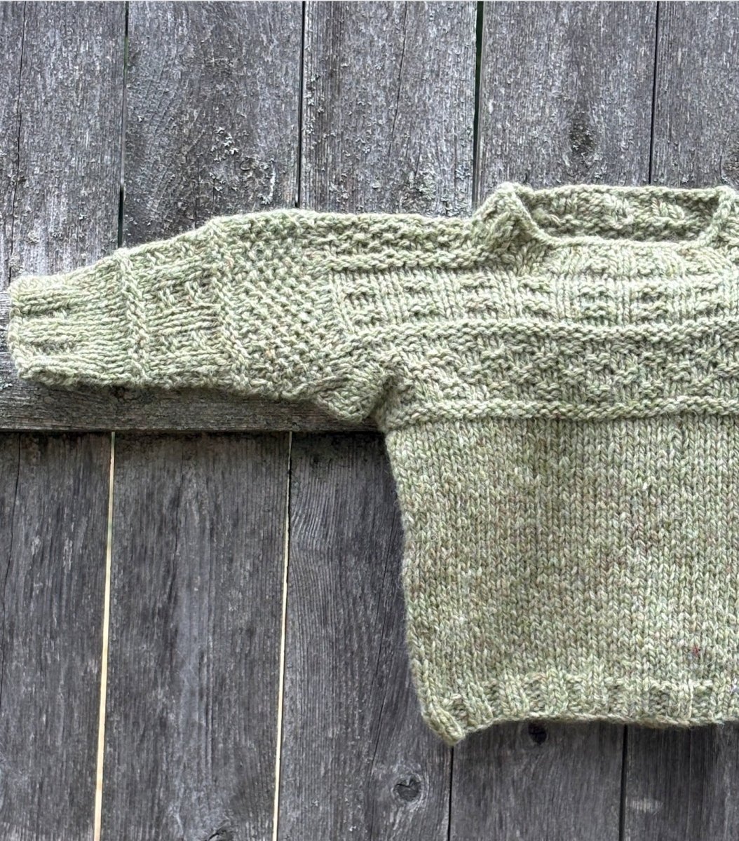 pale green handknit gansey sweather on a weathered wooden background