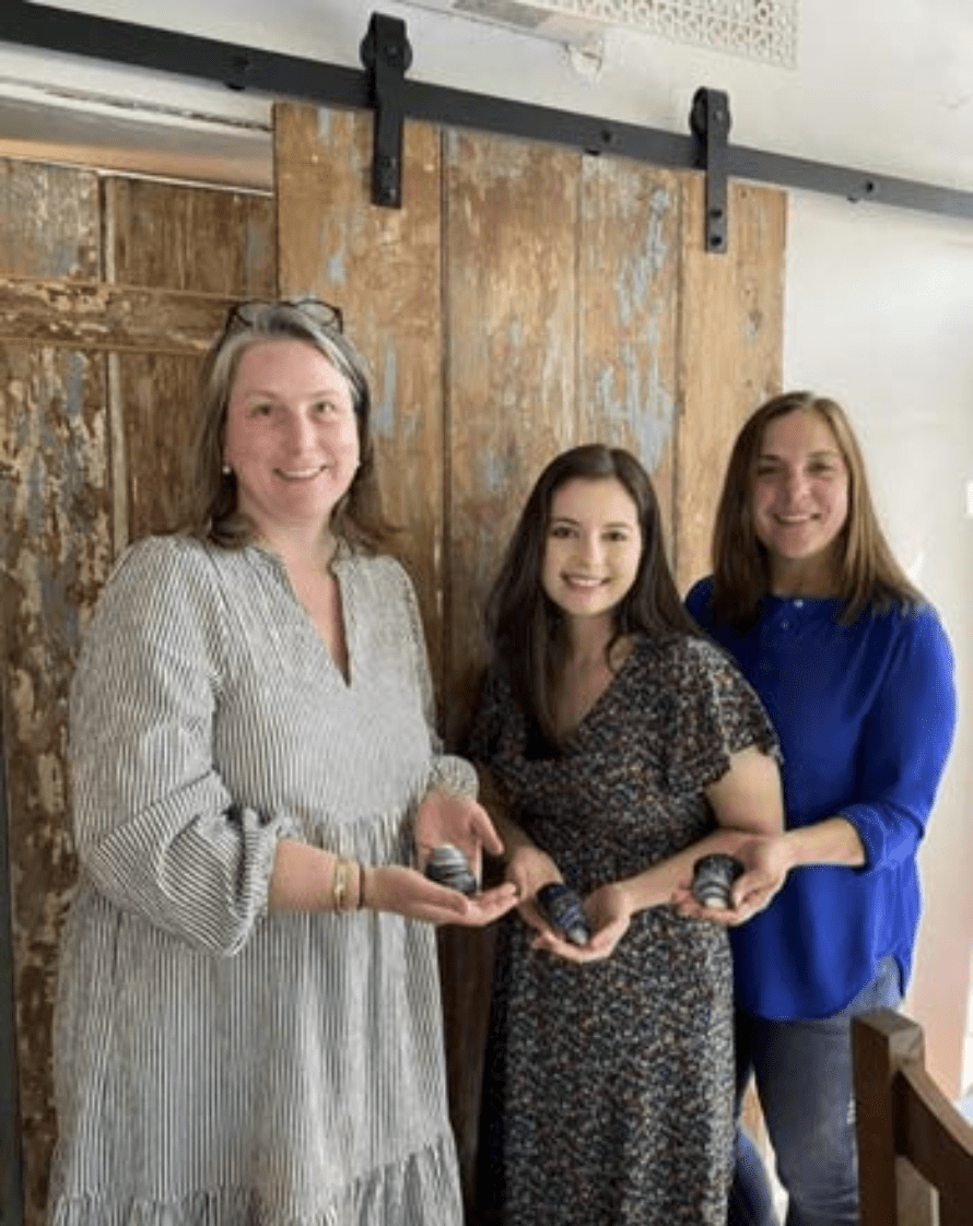 Three women smile indoors, holding dark containers with mussel shell ornaments they made at the Halcyon Yarn Needle Felting Class: Mussel Shells with Michelle Provençal on May 30th.