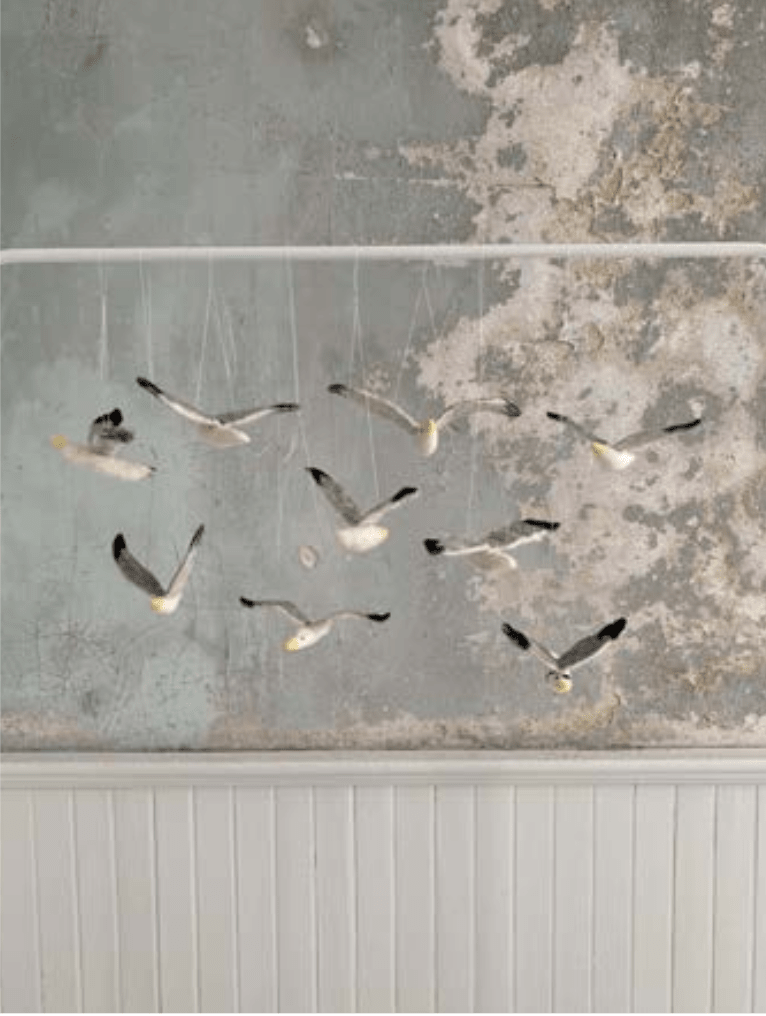 Needle-felted seagulls from Halcyon Yarn’s "Needle Felting Class: Seagull with Michelle Provençal (July 25th)" hang in front of a textured wall, appearing to soar mid-flight and bringing movement and depth to the space.