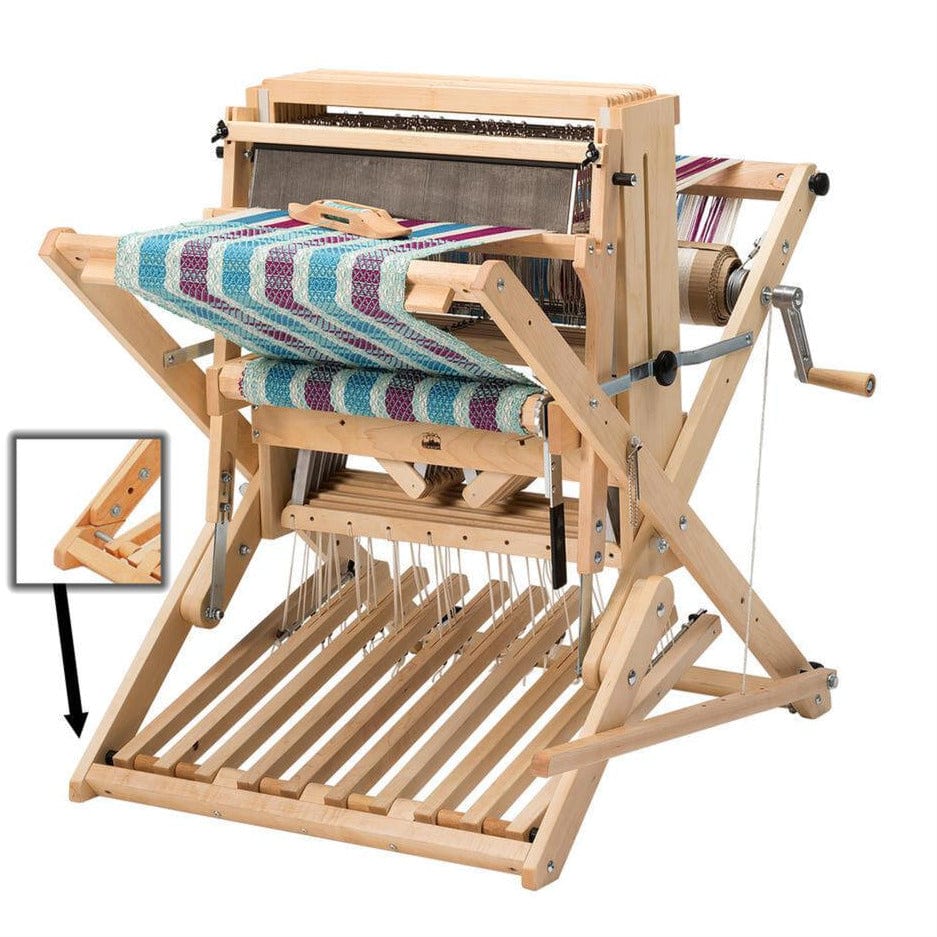 A Schacht Spindle Co. 18″ Wolf Pup Floor Loom with a wooden tabletop and hand crank is shown weaving a blue, purple, and white striped textile. Pedals extend from the base of this portable floor loom, reminiscent of Schacht’s versatile design, while an inset highlights a close-up detail of a wooden joint for added craftsmanship.