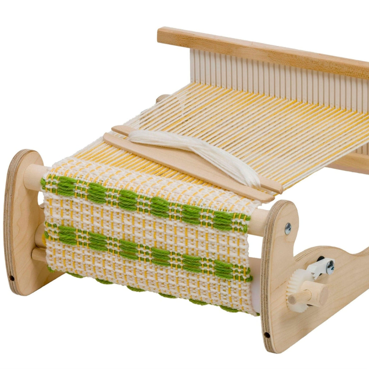A Schacht Cricket Rigid Heddle Loom by Schacht Spindle Co. displays a partially woven fabric in a white and green pattern. Yellow threads are stretched across the loom, and a wooden shuttle with white yarn rests on top.