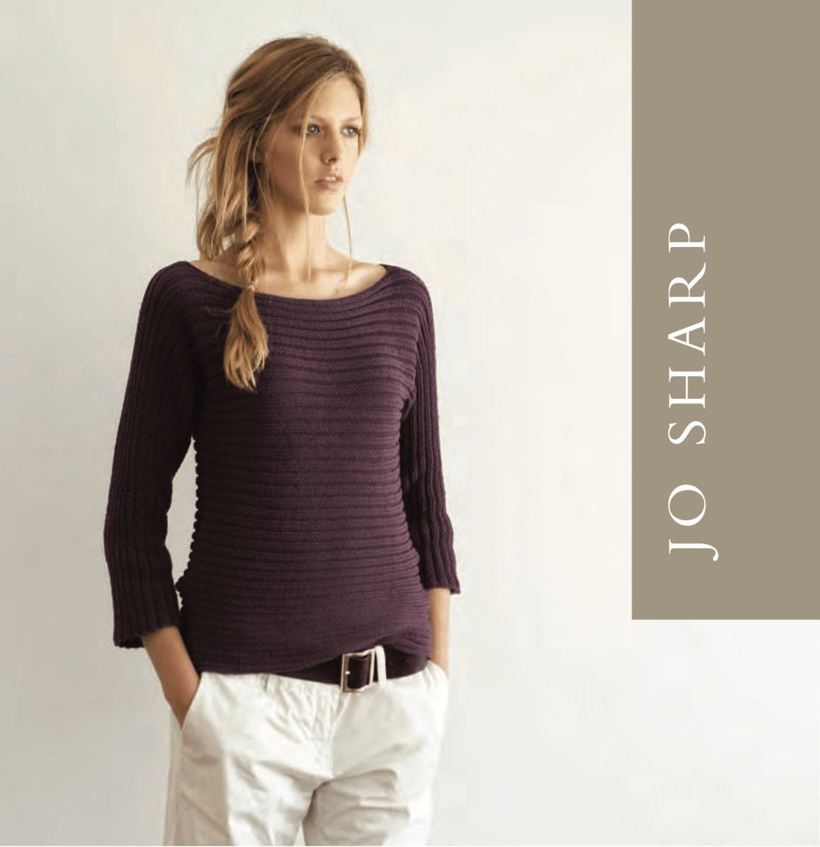 A woman wears a ribbed, dark purple knit sweater—crafted from the Sideways Ribbed Top Pattern by Jo Sharp (print only) from Yankee Knitter Designs—and light pants, with "JO SHARP" vertically displayed on a taupe panel beside her.