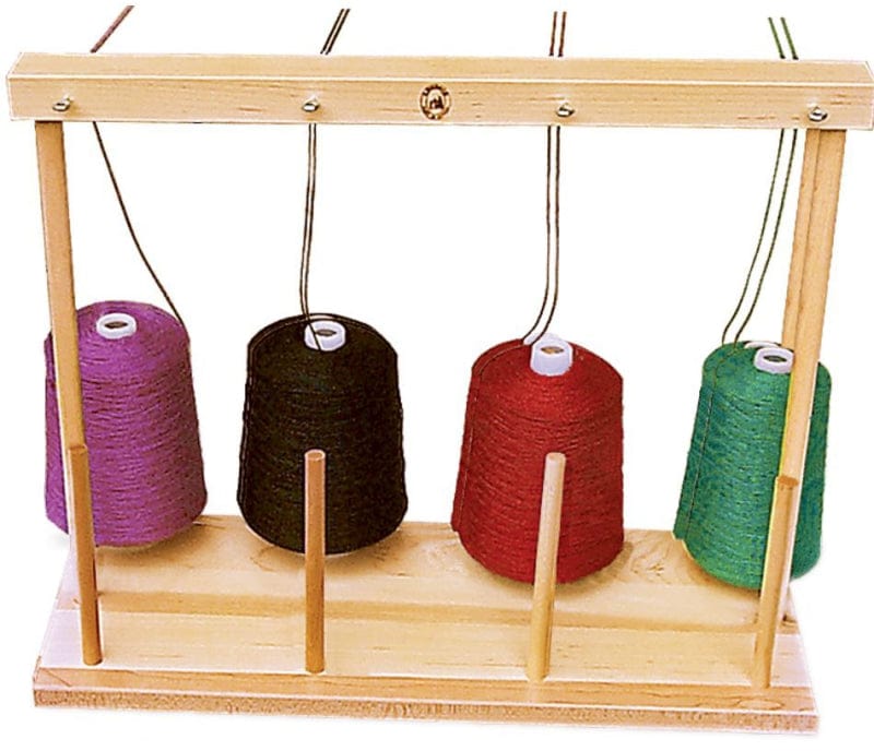 A wooden yarn holder with four upright spools of yarn in different colors: purple, black, red, and green. The holder has wooden pegs aligned to keep the spools in place and wires extending upwards to guide the yarn.