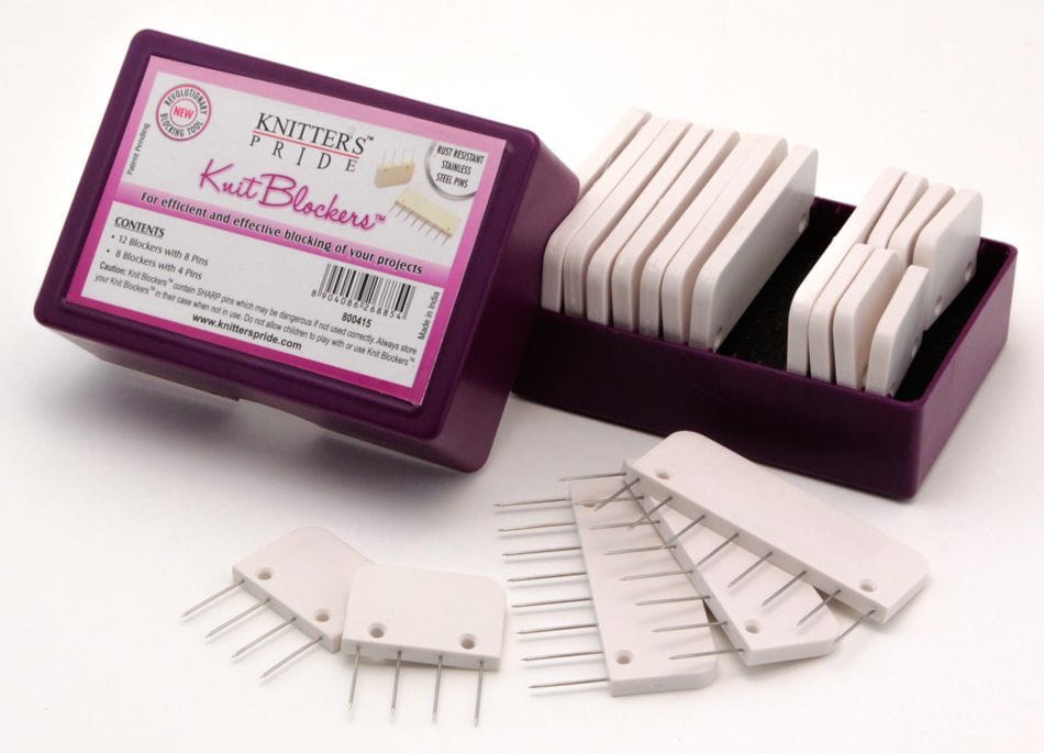 The Knit Blockers by Knit Pro (Knitters Pride) from Accessories Unlimited include white plastic blockers with metal pins in a purple box—ideal for use with your blocking mats. Some blockers are in the box, others displayed in front.