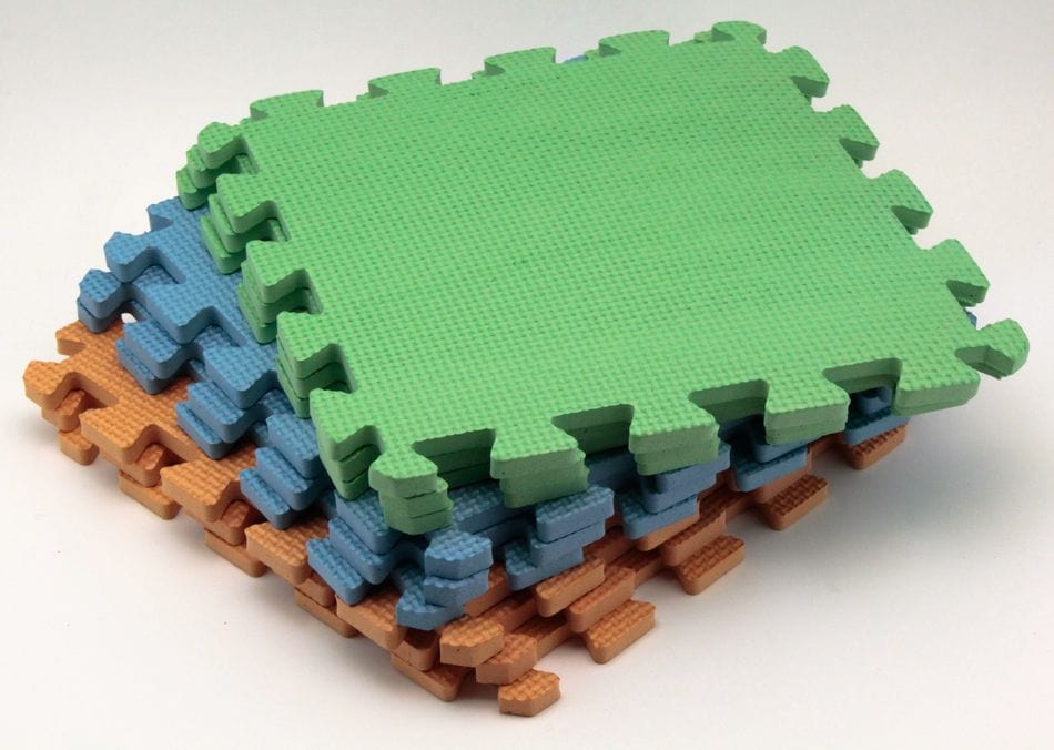 Four interlocking Blocking Mats by Knit Pro (Knit Pro) from Accessories Unlimited are stacked: the top mat is green, the middle two are blue, and the bottom one is brown. These mats feature textured surfaces and puzzle-like edges for easy connection—perfect for crochet blocking or knit blocking projects.