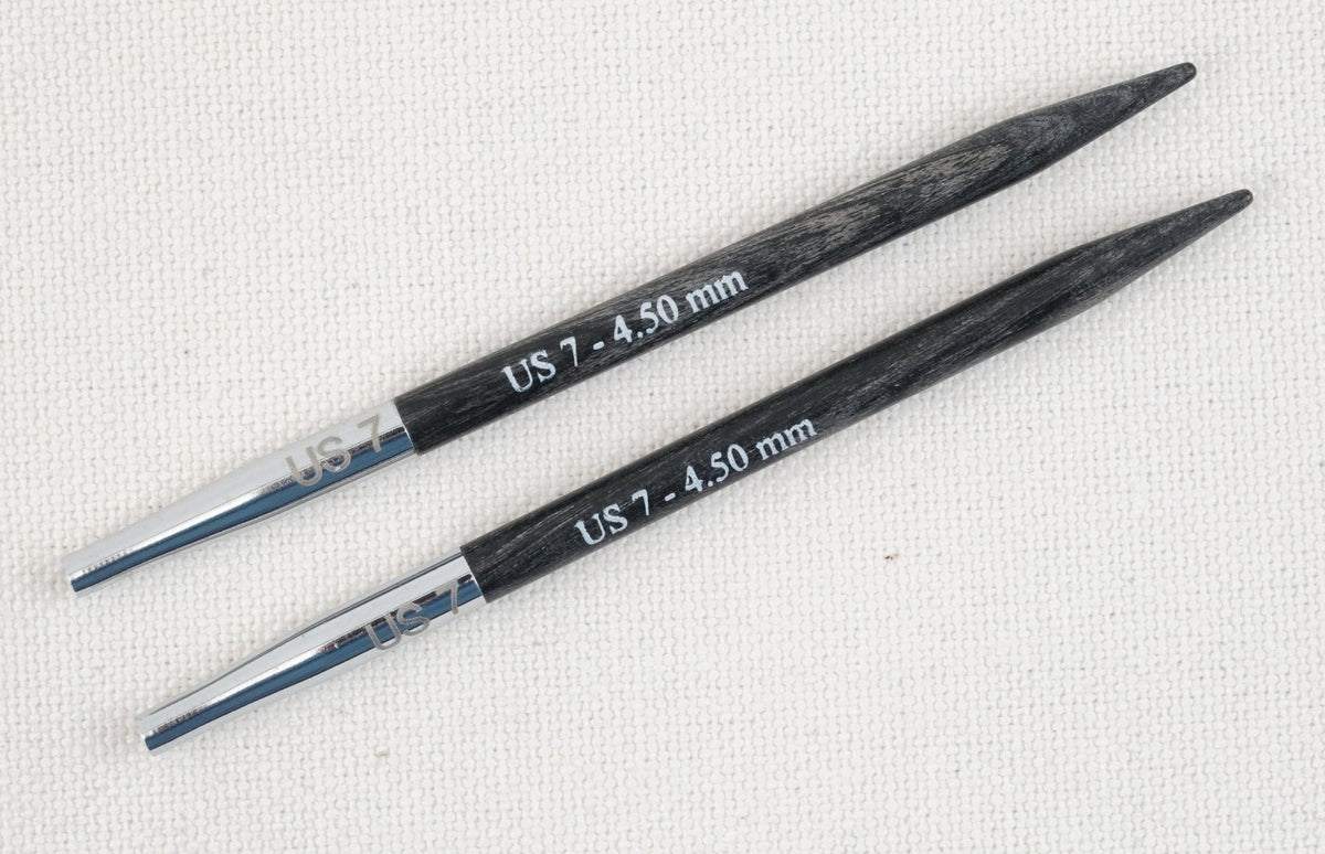 Two black and silver Accessories Unlimited Knit Pro Dreamz Interchangeable Knitting Needle Tips in size US 7 (4.50 mm) are displayed parallel on a light textured fabric background.