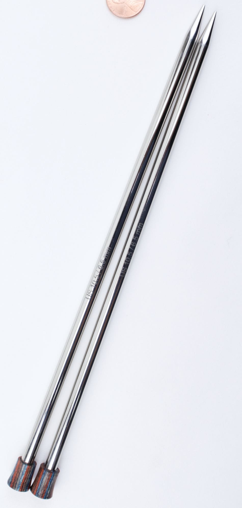 Two Knit Pro (Knitters Pride) Nova Metal Single Point Knitting Needles (10" or 14") by Accessories Unlimited with pointed tips and colorful ends lie parallel on a white surface, with a coin nearby for size comparison.