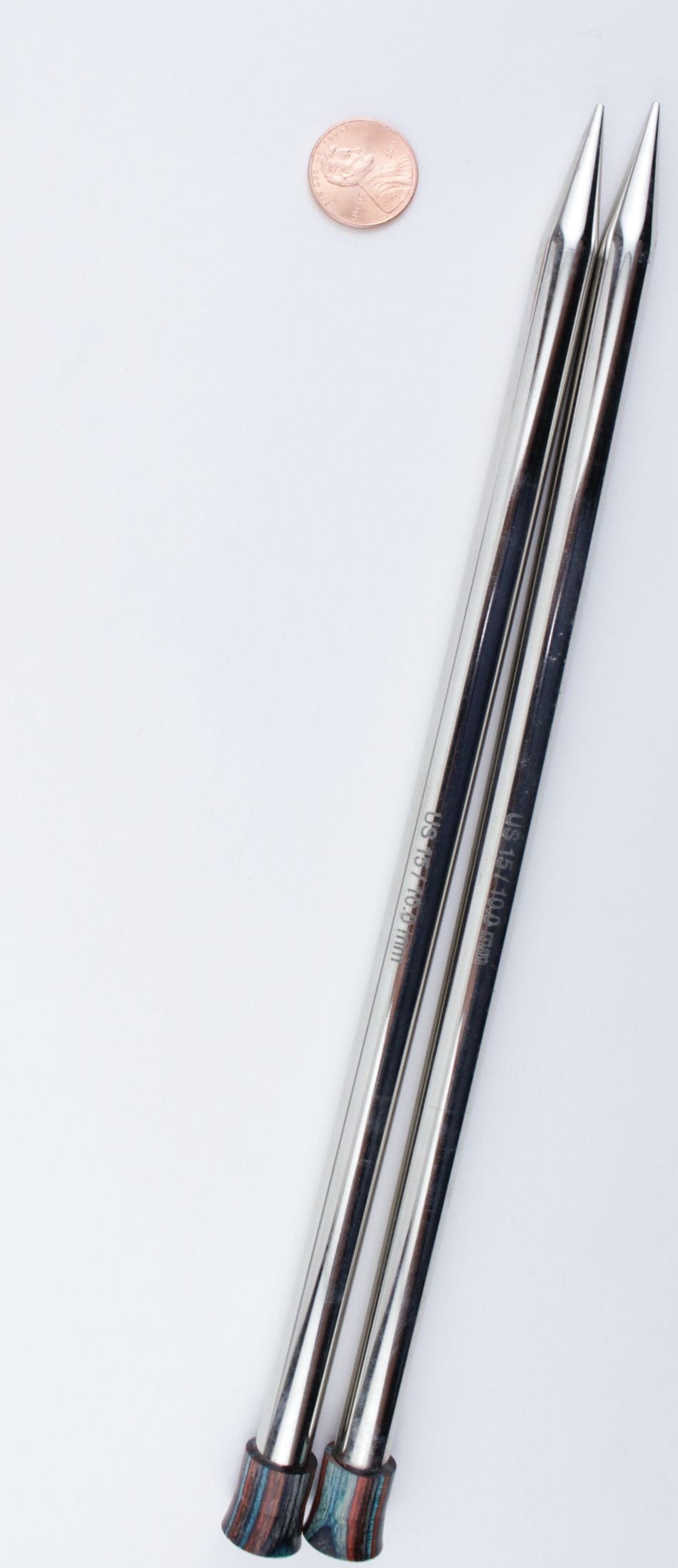 Two Knit Pro (Knitters Pride) Nova Metal Single Point Knitting Needles by Accessories Unlimited (10" or 14") with decorative ends are set side by side on a white surface, a penny placed above them for size comparison.