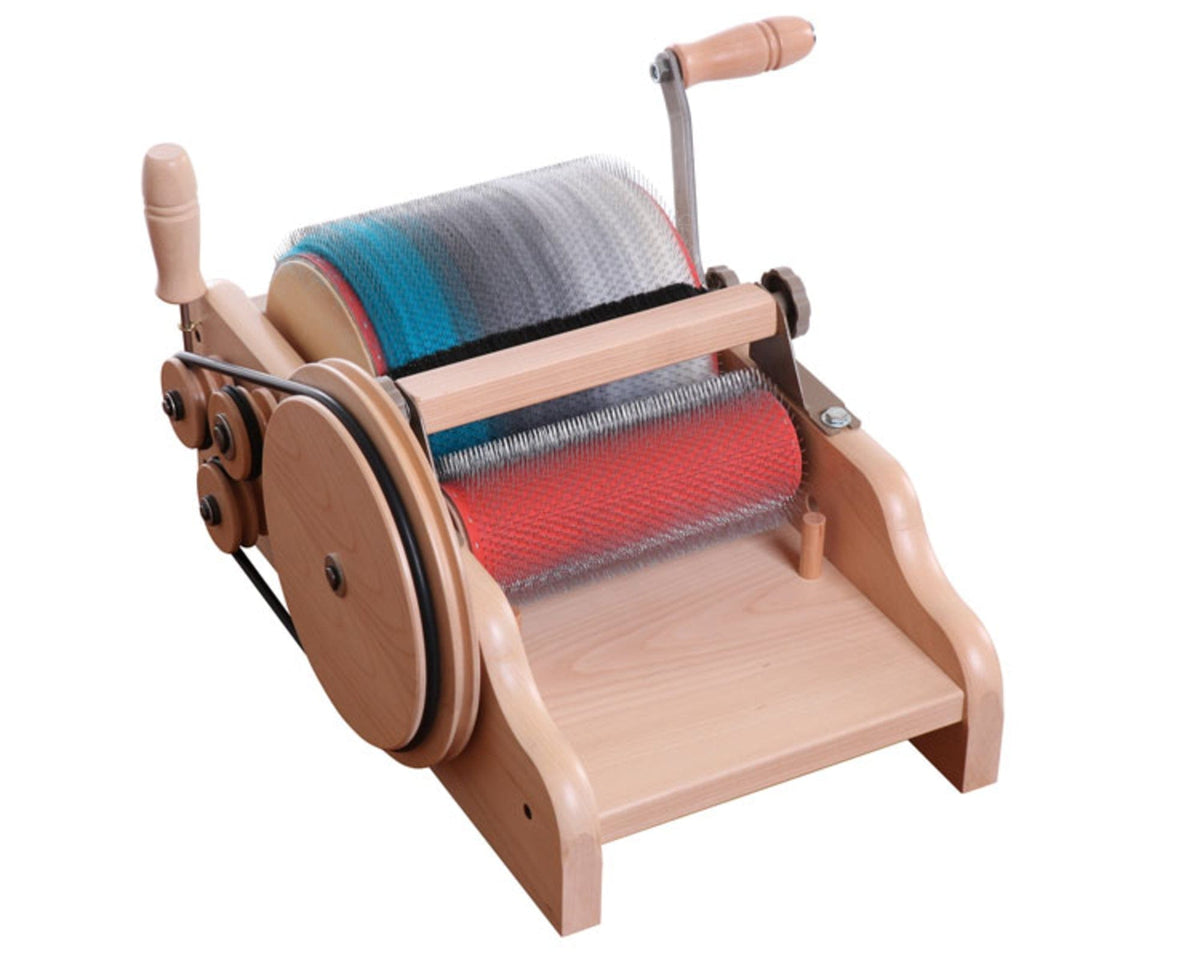 The Ashford Drum Carder by Ashford Handicrafts Limited blends and prepares fibers for spinning, featuring two metal-toothed rotating drums, a flat wooden base, and a hand crank.